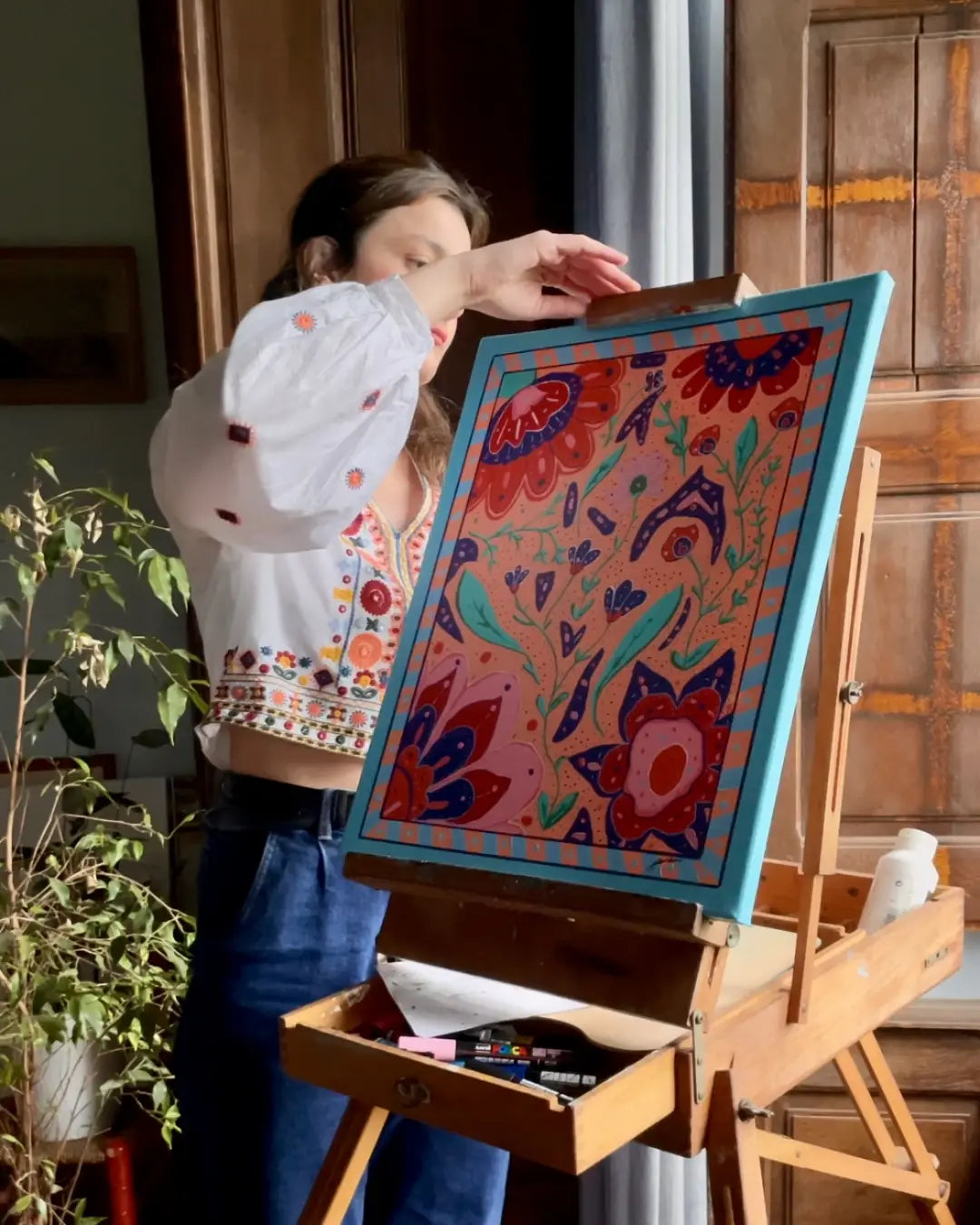 L'artiste peintre Blandine Cavalier, fixe sa toile Carnaval, Flowers, 2025, sur sn chevalet, dans son atelier.